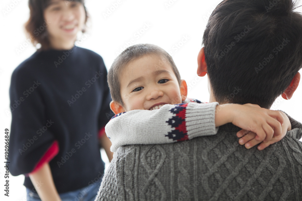 お父さんに抱きついて甘えている男の子。見守るお母さん。