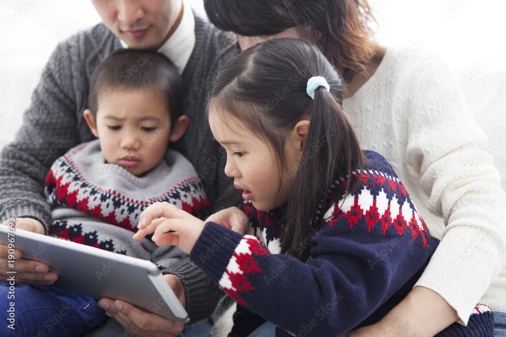 お父さんとお母さんが笑顔で話している。タブレットを見ている娘と息子。