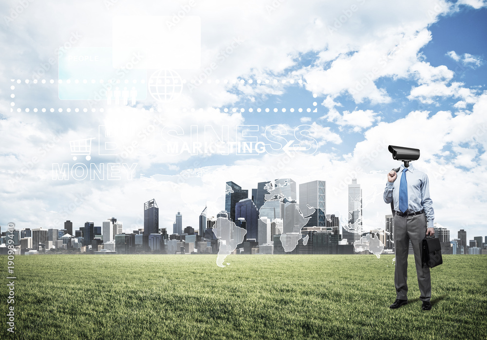 Camera headed man standing on green grass against modern citysca