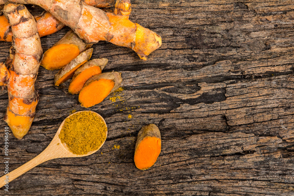 turmeric powder in spoon and roots on wooden plate