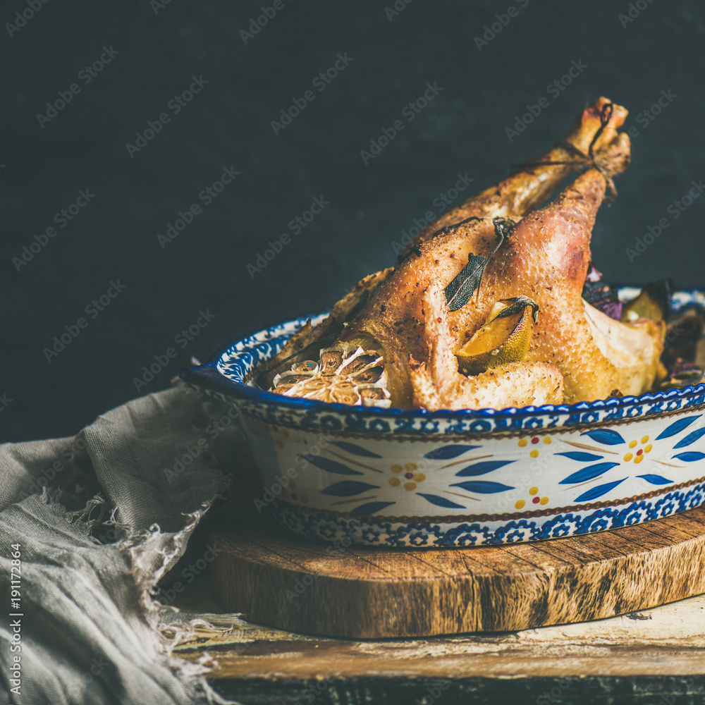 Roasted whole chicken for Christmas eve celebration table on rustic wooden board, black wall backgro