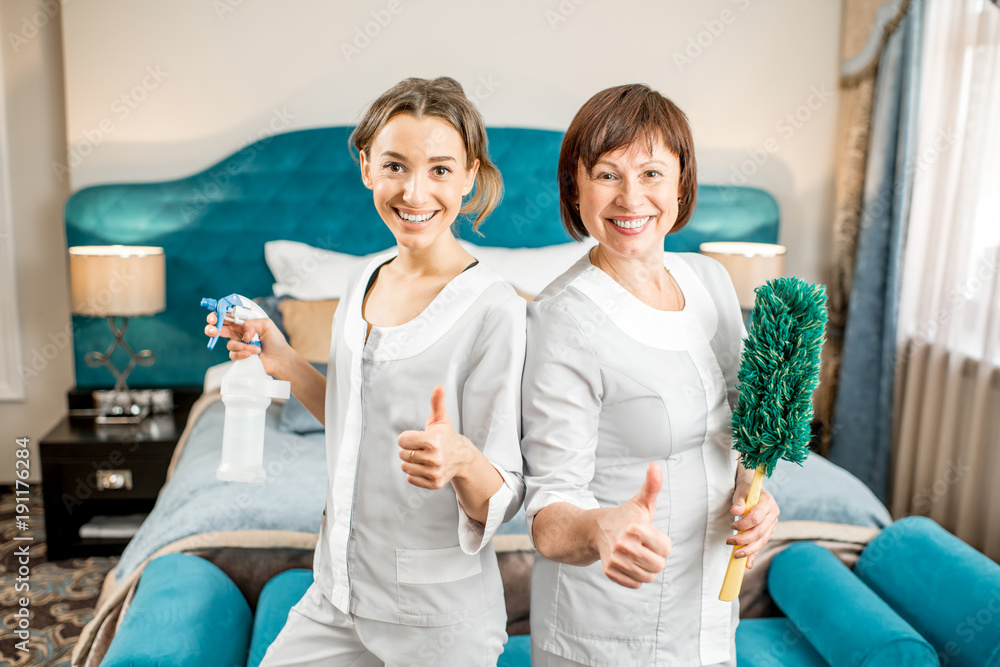 Portrait of a senior chambermaid with young assistant in uniform standing in the luxury hotel bedroo