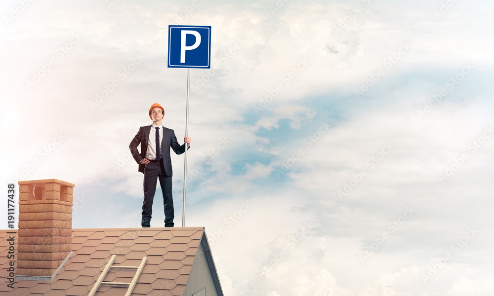 Young businessman with parking sign standing on brick roof. Mixe