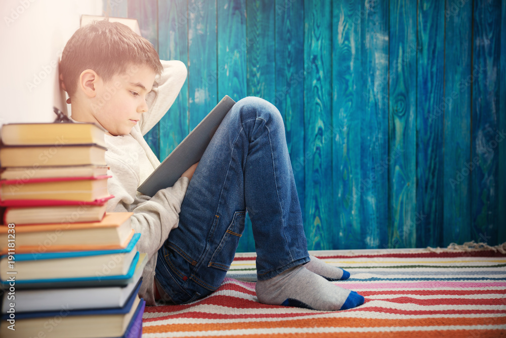 eight years old child reading a book at home. Boy studying on blue background