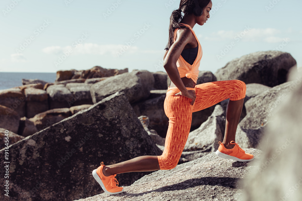 Female runner stretching legs on rocks