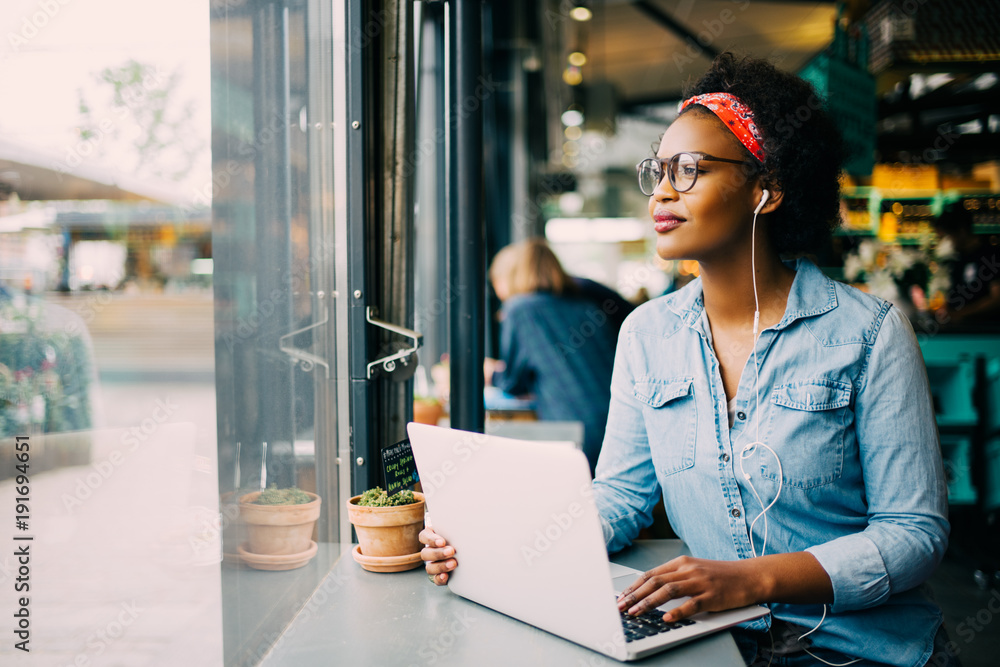 Smiling young African woman working online by a cafe window