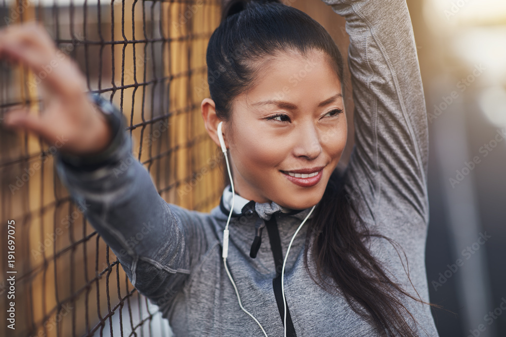 Sporty Asian woman leaning against a mesh wall before jogging