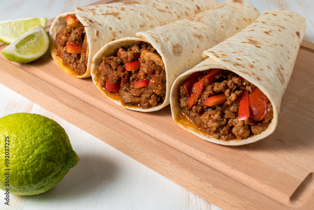 Tasty homemade burrito with vegetables and beef on wooden background.