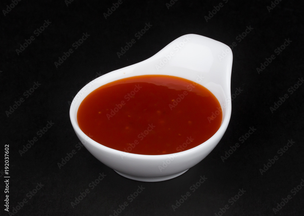 Hot chilli sauce in white bowl isolated on black background