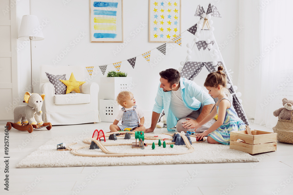 family father and children play a toy railway in   playroom.