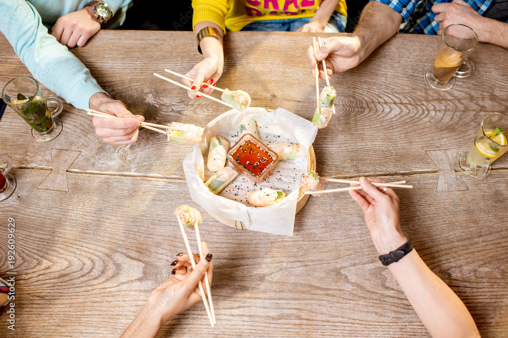 用棍子吃米饭卷，米饭卷上放着虾和酱汁，放在木板上，标签上放着纸