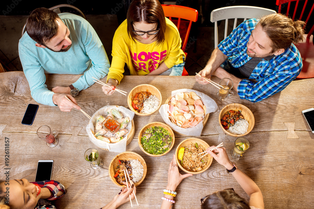 Top view on the table full of different asian meals served in the wooden plates and young people eat