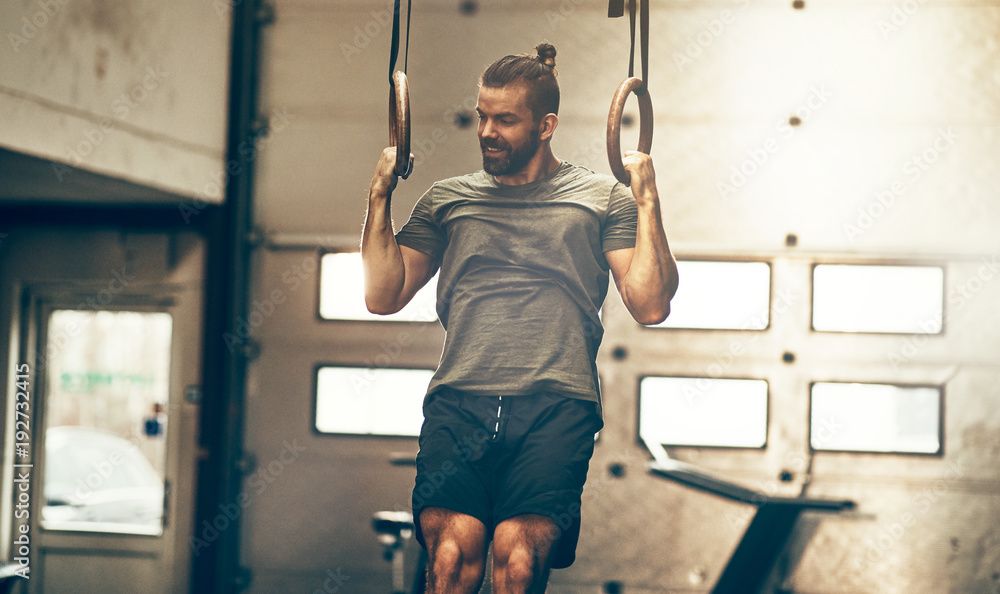 Muscular young man working out on rings at the gym