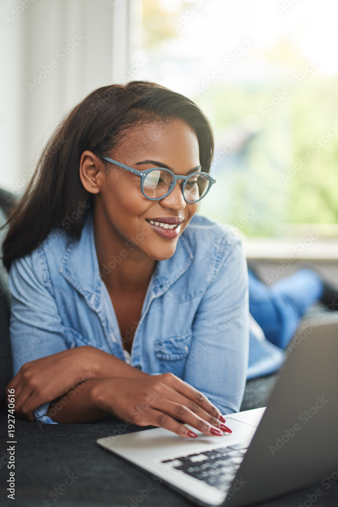 Young African woman lying on her sofa working online