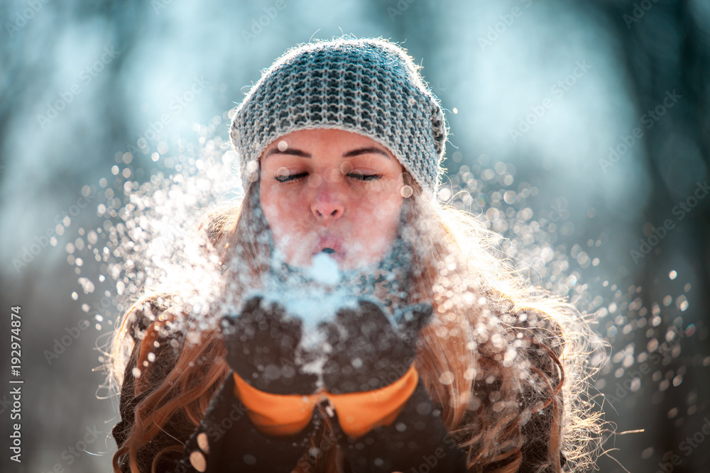 冬日女人在阳光明媚的日子里在户外吹雪，雪花纷飞