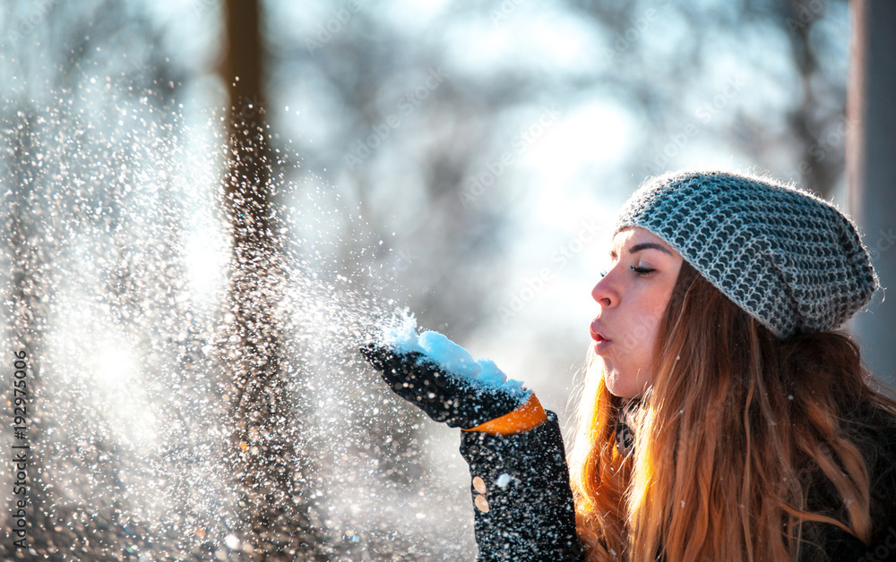 冬日女人在阳光明媚的日子里在户外吹雪，雪花纷飞