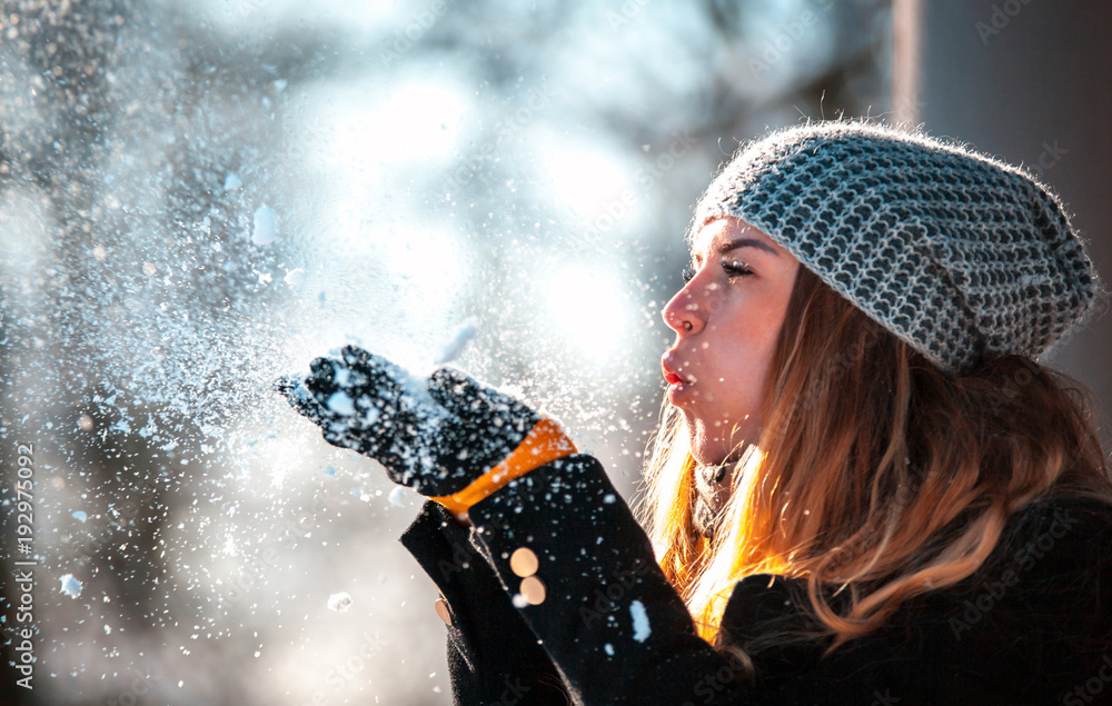 冬日女人在阳光明媚的日子里在户外吹雪，雪花纷飞