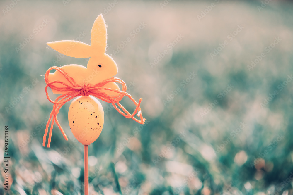 Easter background concept with yellow bunny figure and egg on wood stick in green grass