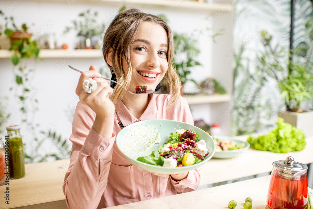 Young woman sitting with healthy food in the beautiful interior with green flowers on the background