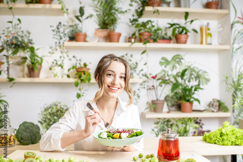 年轻女子坐在美丽的室内吃健康食品，背后开着绿色的花朵