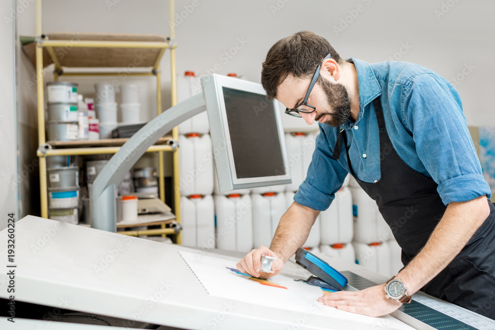 Worker checking the quality of the printing with magnifying glass on the operating table of the prin