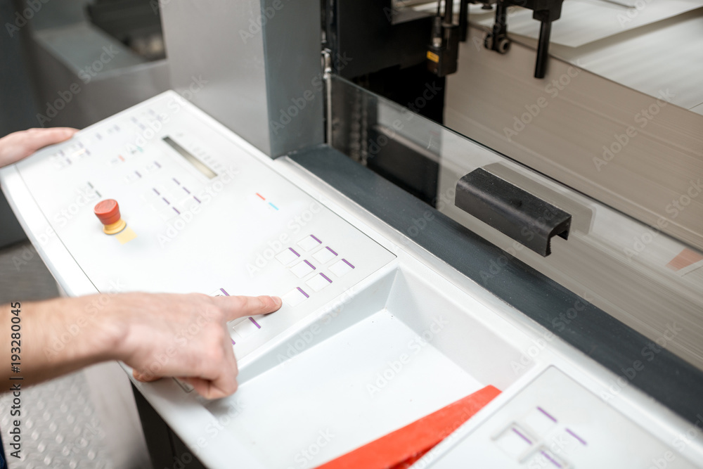 Man operating offset machine pushing the button at the printing manufacturing. Close-up view