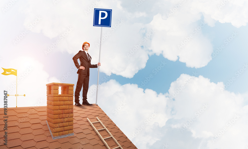 Young businessman with parking sign standing on brick roof. Mixed media