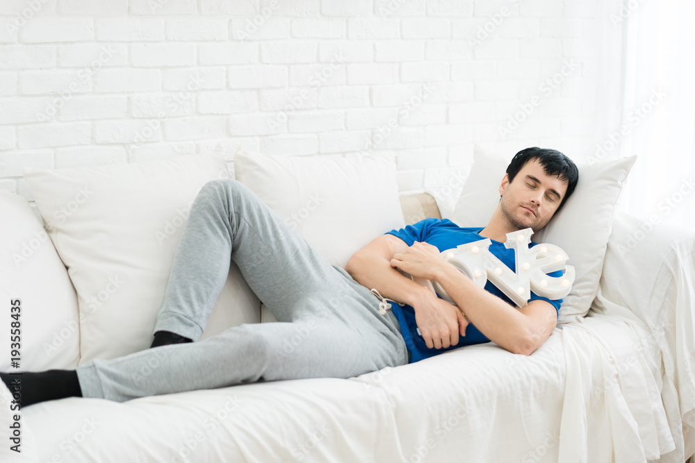 Young handsome man slepping and hugging LOVE alphabet in sofa in bedroom at home. Young single man w