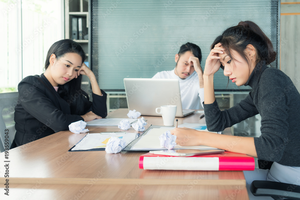 一群穿着休闲西装、闷闷不乐的亚洲商务人士坐在商务会议室里，看起来很糟糕