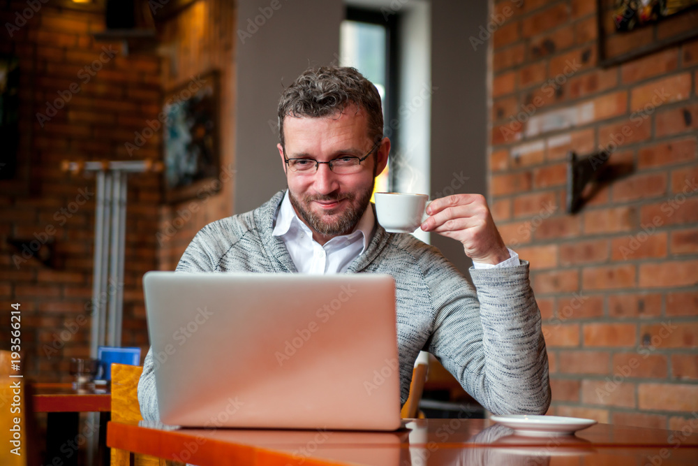 Middle age man using laptop in cafe and drinking coffee