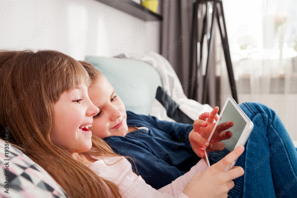 Happy children on sofa at home playing with digital tablet together