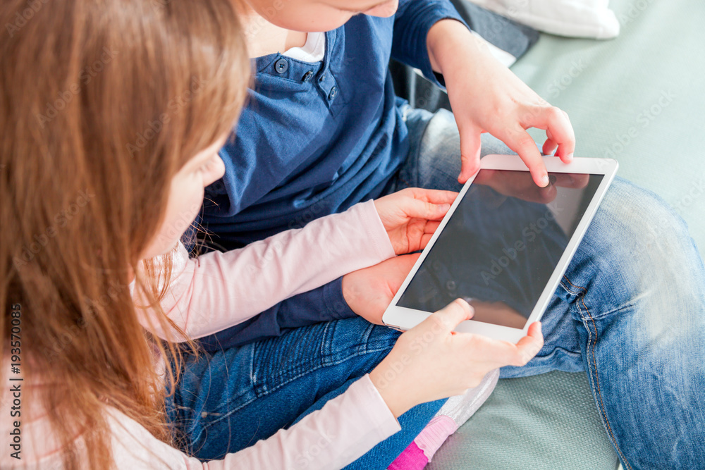 Happy children on sofa at home playing with digital tablet together