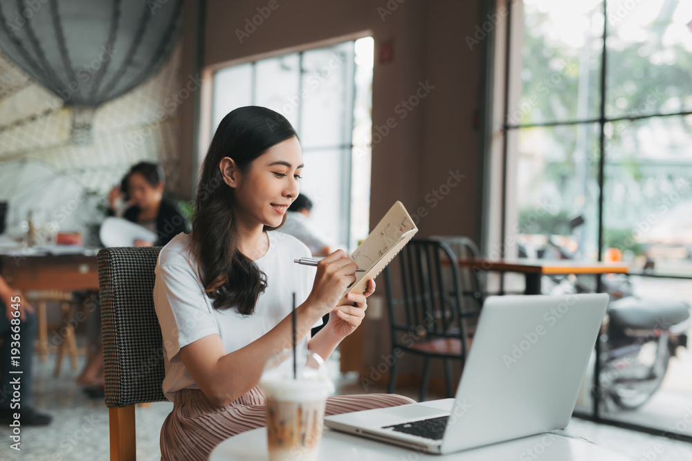 年轻的商务女性坐在桌子旁，在笔记本上做笔记