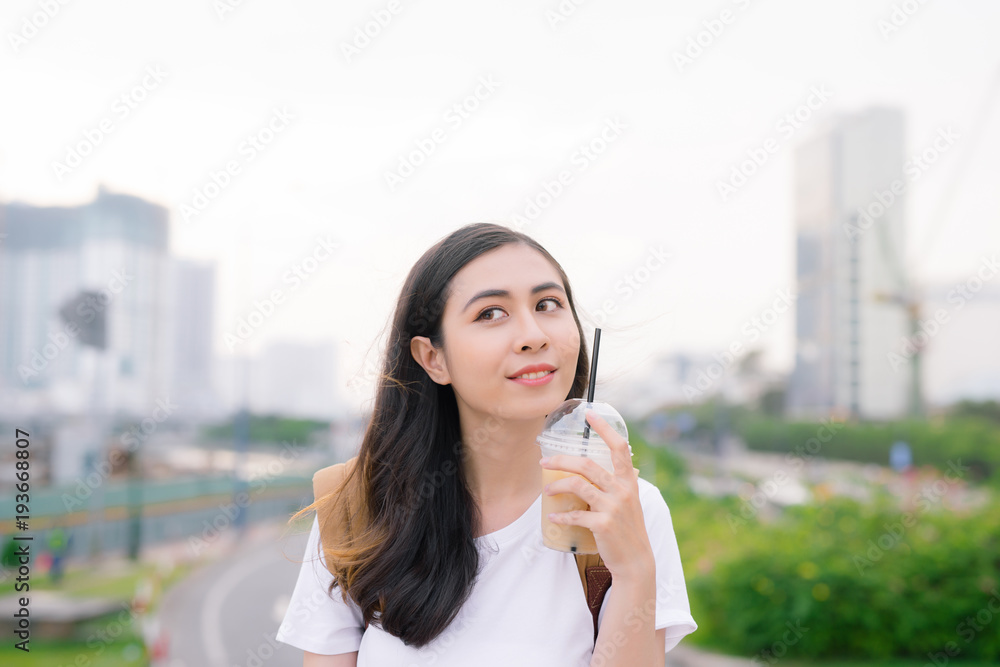 年轻漂亮的女孩站在桥上，手里拿着咖啡杯，可以看到城市的景色。