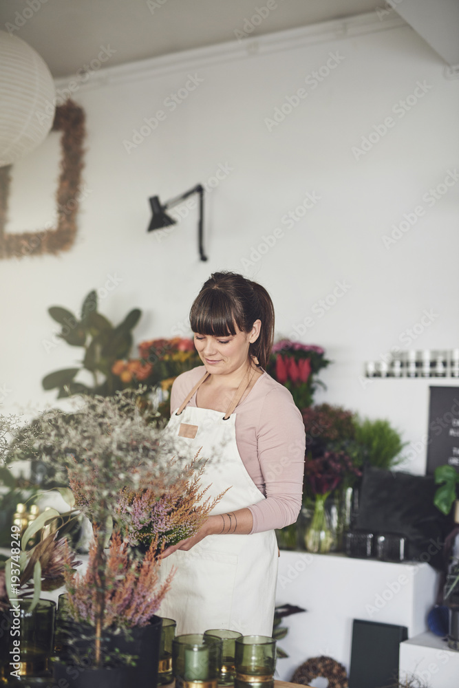 Smiling female florist standing in her shop arranging flowers