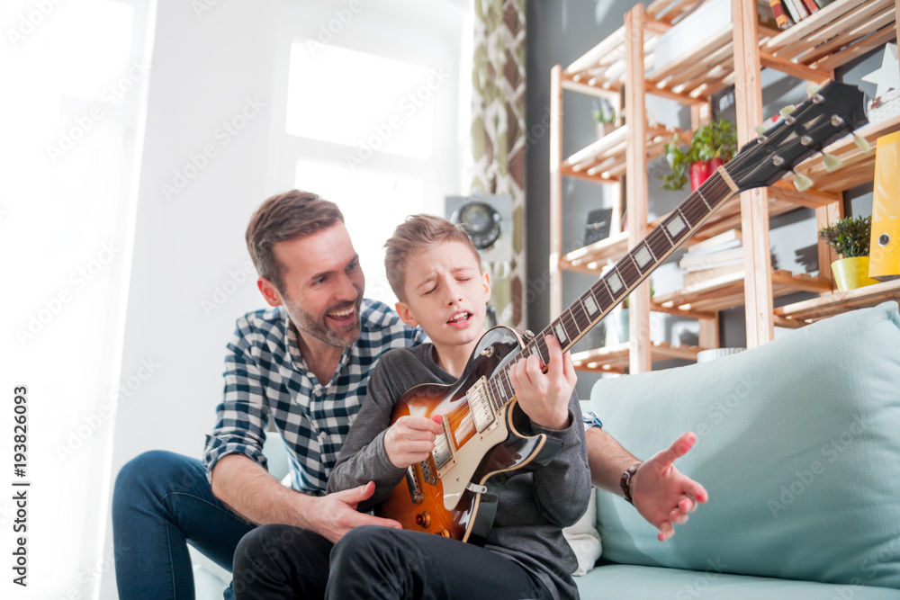 Son and father playing electric guitar at home