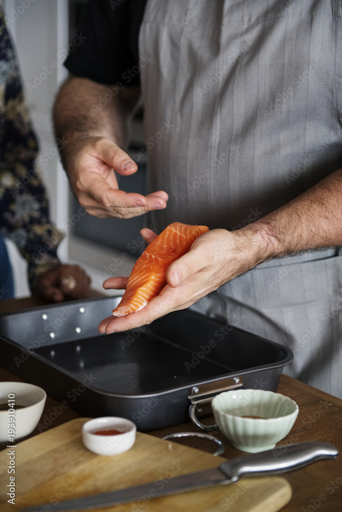 Woman adding spices and herb to raw salmon