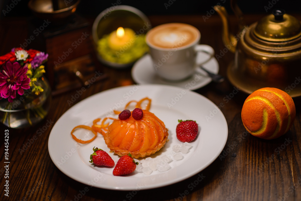 Restaurant cuisine, peach dessert with strawberries, near orange and cappuccino