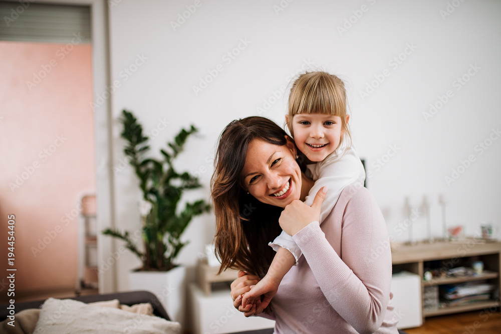 Image of a happy mother piggybacking adorable little daughter. Looking at camera