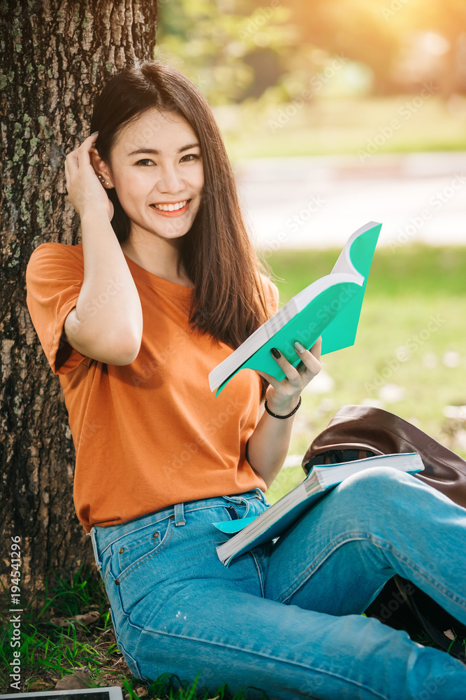 一个年轻或十几岁的亚洲女学生在大学里微笑着看书，看着平板电脑