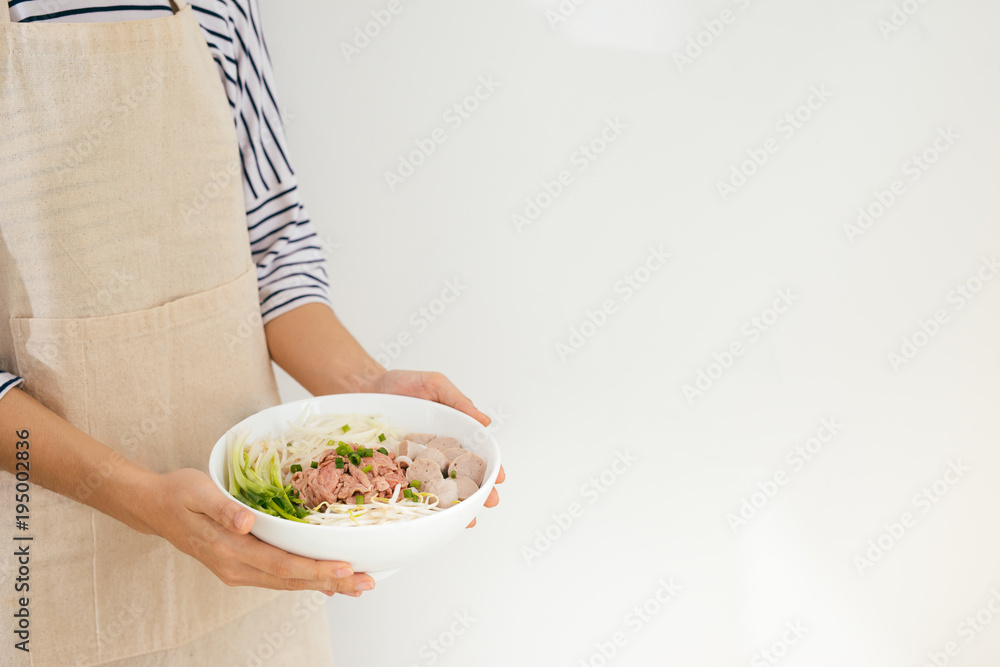 Female chef prepare traditional Vietnamese soup Pho bo with herbs, meat, rice noodles