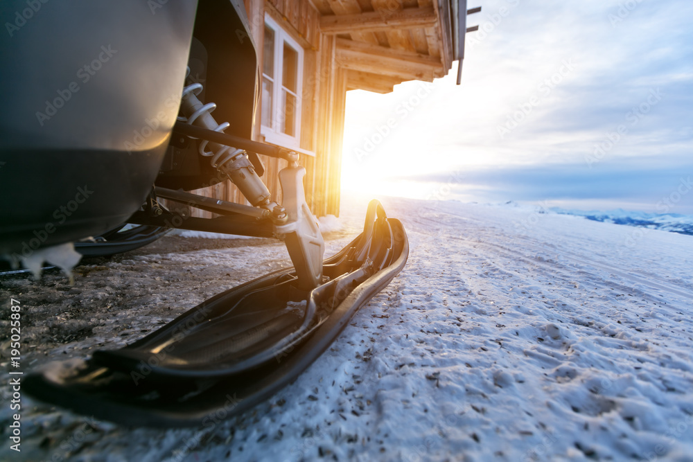 Closeup of snowmobile parking next to log cabin