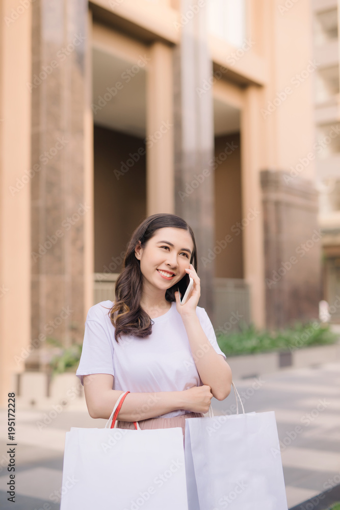 漂亮女孩拿着购物袋，用的是智能手机