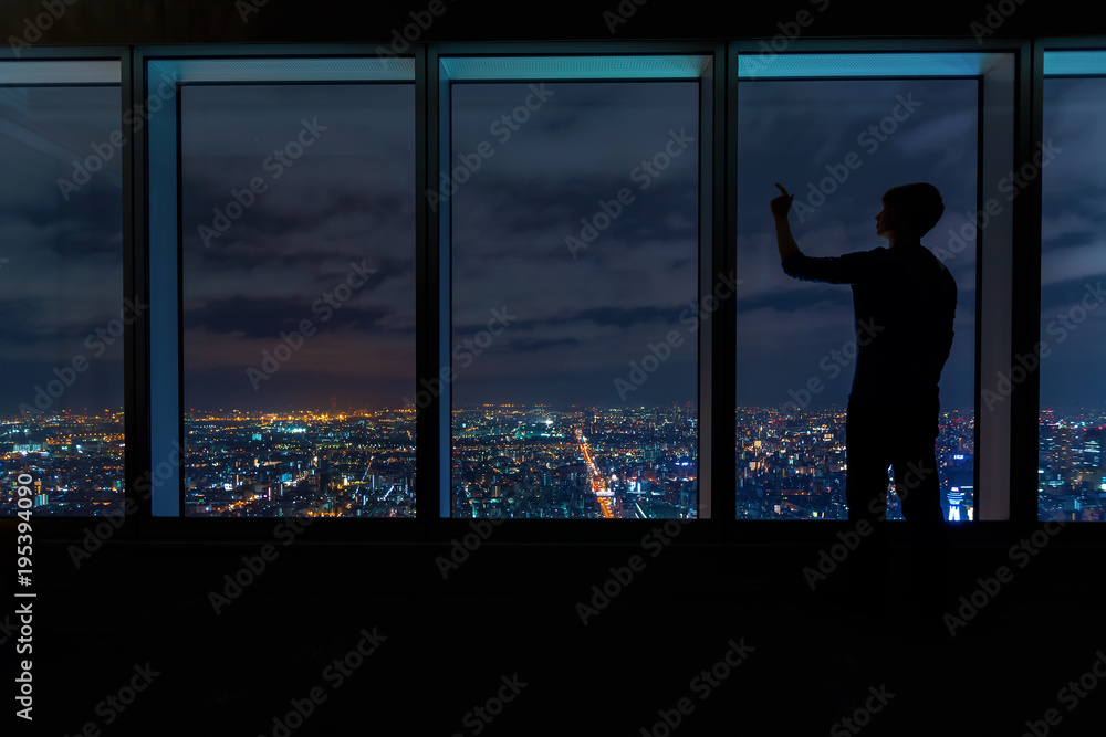 一名男子在夜晚从一座庞大的城市上空的大窗户向外张望