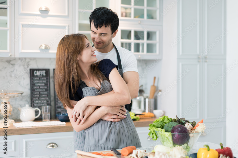 可爱的年轻夫妇在现代厨房准备健康的饭菜。早上男人拥抱女人浪漫