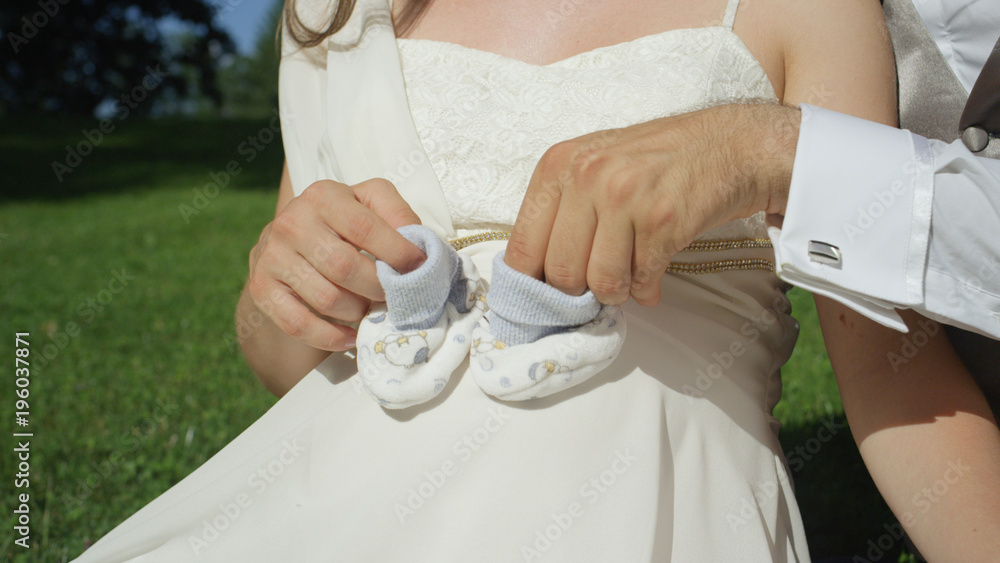 特写：兴奋的父亲把一双婴儿袜套在怀孕的肚子上