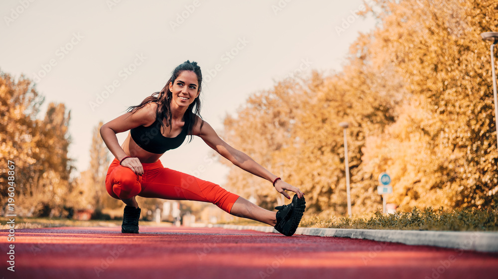 Young fit woman stretching on tartan track before run.