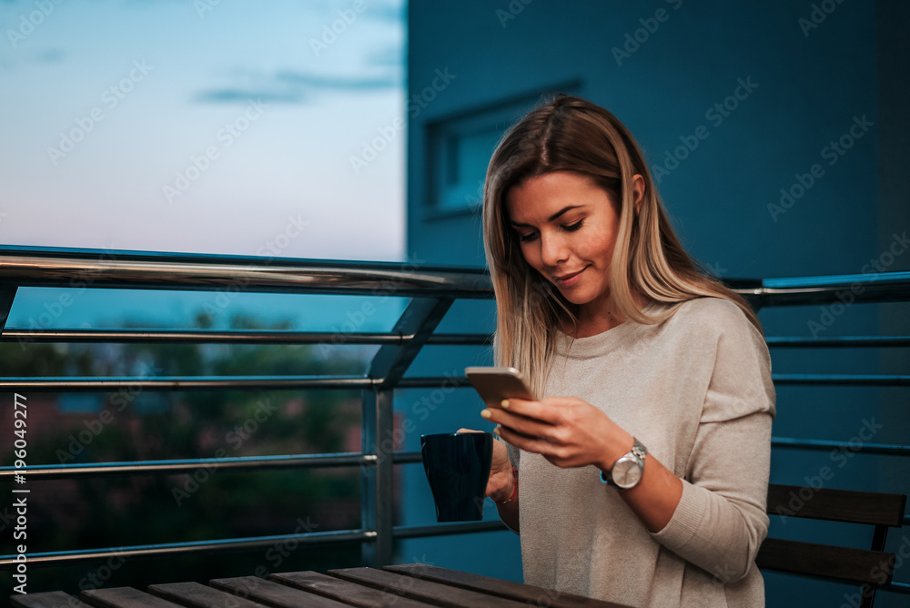 Image of smiling woman using smartphone while drinking tea or coffee on teracce.