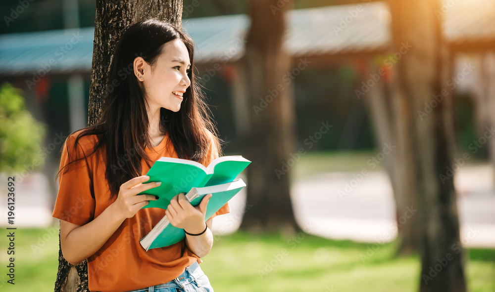 一个年轻或十几岁的亚洲女学生在大学里微笑着看书，看着平板电脑