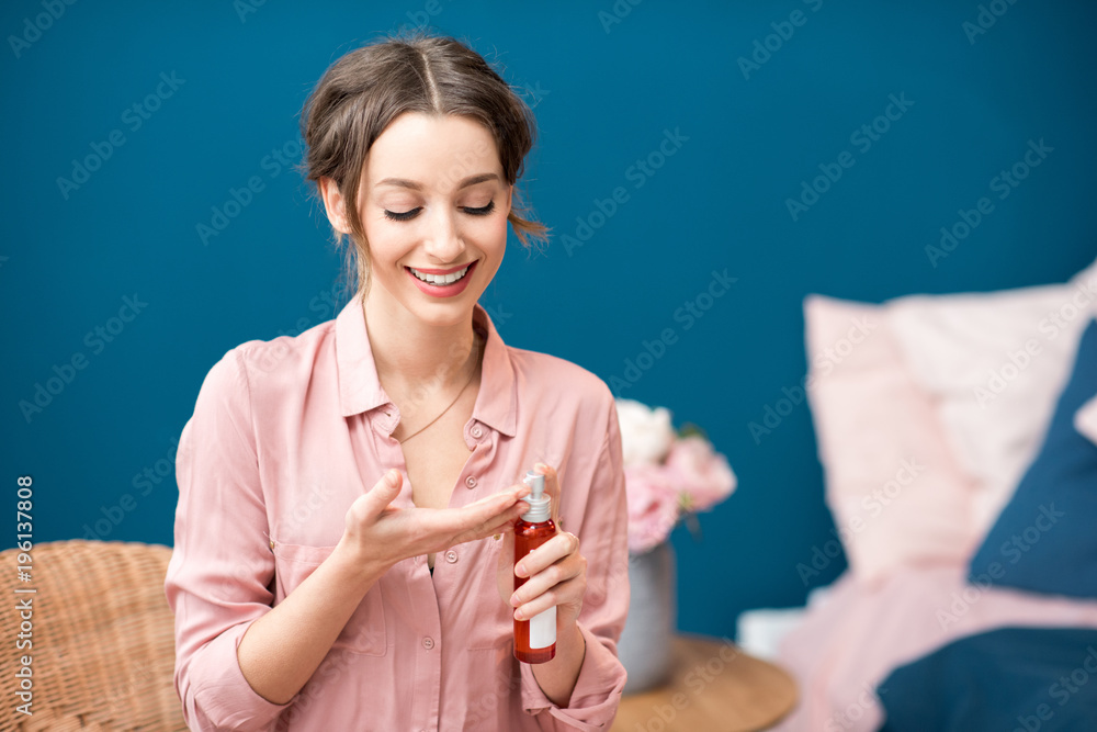 Young woman putting cream on the hand sitting on the blue wall background at home